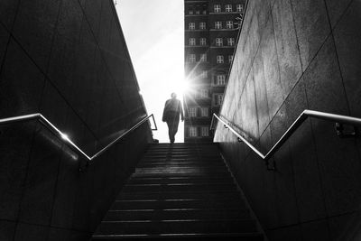 Rear view of man walking on staircase amidst buildings in city