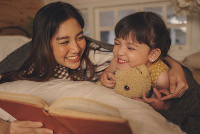 Mother and girl reading book while relaxing on bed