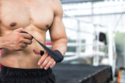 Midsection of shirtless man tying armband