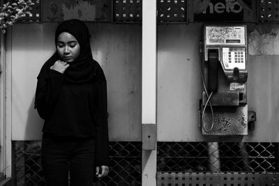 Thoughtful young woman standing by pay phone