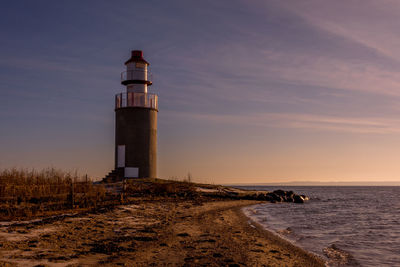 Lighthouse by sea against sky during sunset