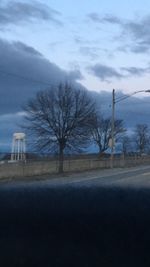 Bare trees by road against sky