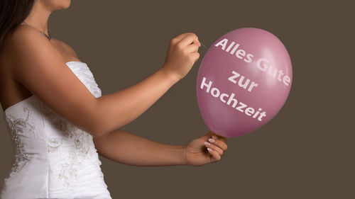 Midsection of bride holding balloon and needle against gray background