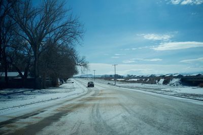 Road by snow covered landscape against sky