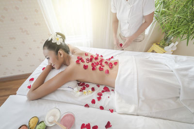 Shirtless young woman with rose petals lying on massage table at spa