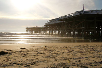 Pier on beach against sky during sunset