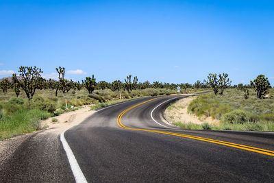 Road passing through landscape against clear blue sky