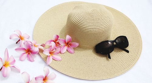 High angle view creme colour woman summer straw hat with sun glasses and pink plumelia flowers.