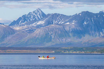 People rowing boat in lake against rocky mountains