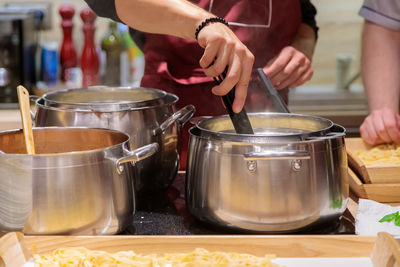 The chef prepares pasta in large metal pans. male hands take out the pasta from the pan with tongs.