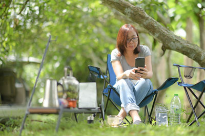 Woman with smartphone during camping, wearing glasses and gray t-shirt.