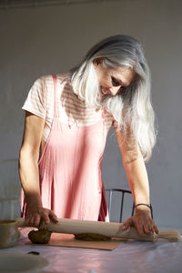 Smiling mature woman rolling clay with pin