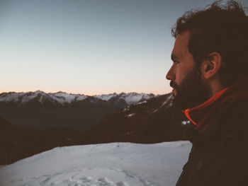 Side view of man looking at snowcapped mountains during sunset