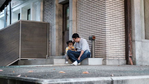 Full length of man sitting on wall in city