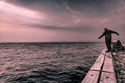 Man standing in sea against sky during sunset