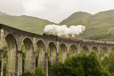 View of steam train on bridge against mountain