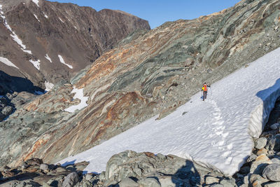 Man climbing on snow covered mountains against sky