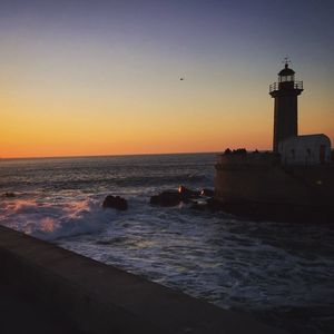 View of lighthouse at seaside during sunset