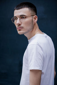 Young man looking away while standing against blue background