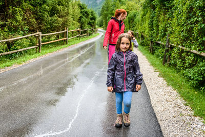 Full length of family walking on wet road amidst trees