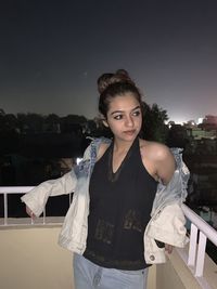 Portrait of young woman standing against sky at night