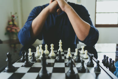 Midsection of man playing chess on table at home