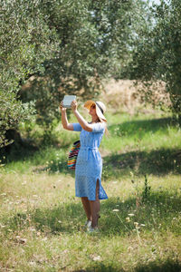 Full length of woman photographing with digital tablet outdoors