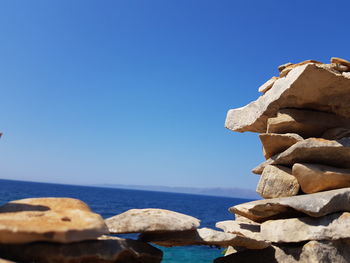 Stack of rocks by sea against clear blue sky