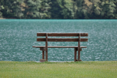 Empty bench on grass against lake at park