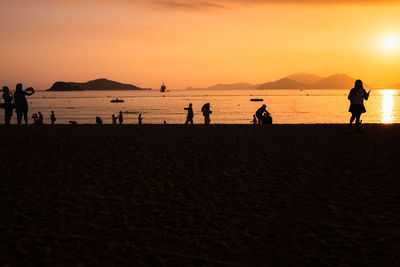 Silhouette people on beach against sky during sunset