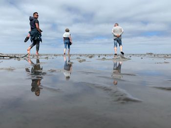 Rear view of people at beach against sky