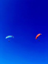 Low angle view of people paragliding against clear blue sky