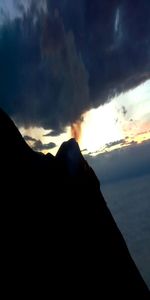 Silhouette mountain by sea against sky during sunset