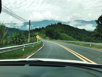 Road by mountains against sky seen through car windshield