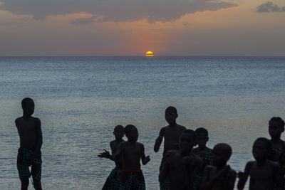 Silhouette people on beach against sky during sunset