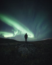 Rear view of man standing on rock at night