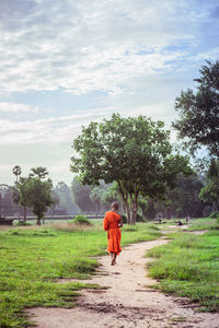 Rear view of young man in traditional clothing walking on trail against cloudy sky