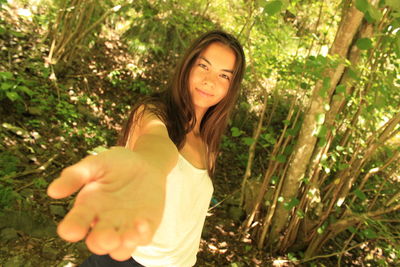 Portrait of smiling young woman gesturing while standing against trees in forest
