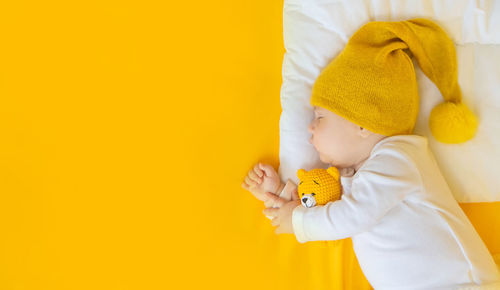 High angle view of baby boy with teddy bear against yellow background