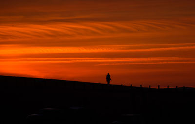 Silhouette person standing on field against orange sky