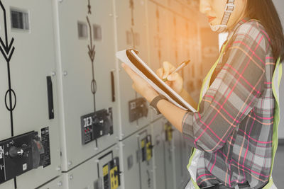 Midsection of female worker examining machinery in factory