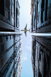 Directly below shot of airplane flying over buildings against sky