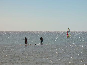 People paddleboarding on sea against sky