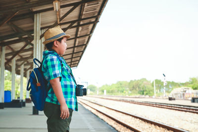 Side view of boy standing by railroad tracks against sky