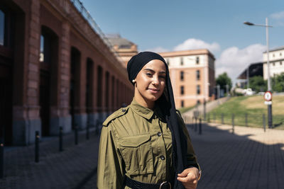 Portrait of young woman standing against buildings