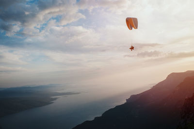 Person paragliding over mountains against sky