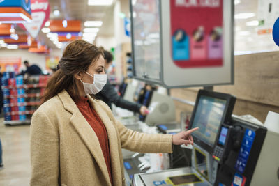 Woman wearing mask using atm at mall