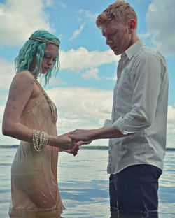 Side view of young couple standing in sea against sky