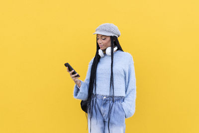 Woman using smart phone in front of yellow wall