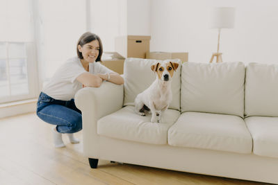 Woman with dog crouching by sofa at home